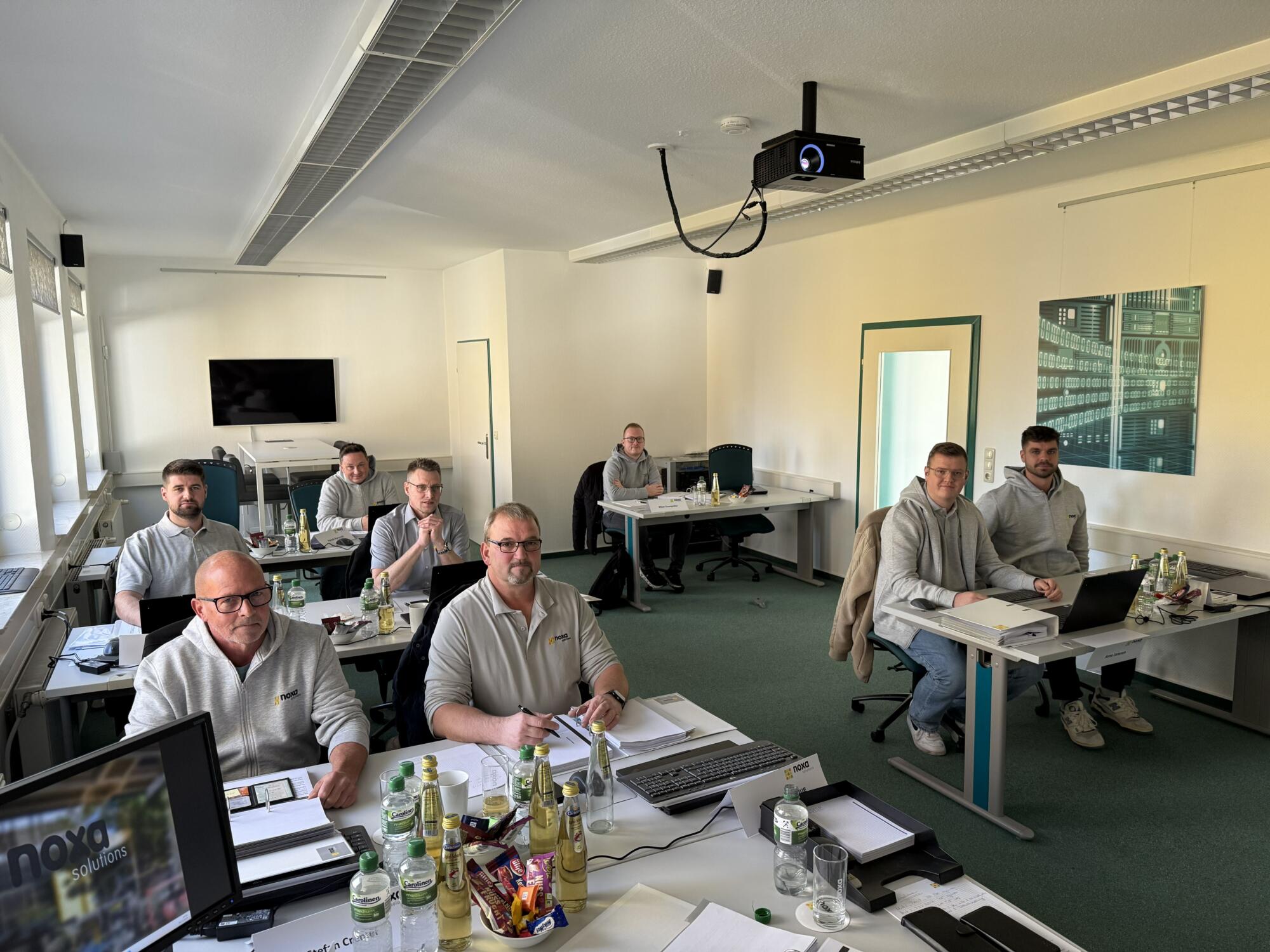 Das Bild zeigt die neuen Mitarbeiter von November am Schreibtisch sitzen